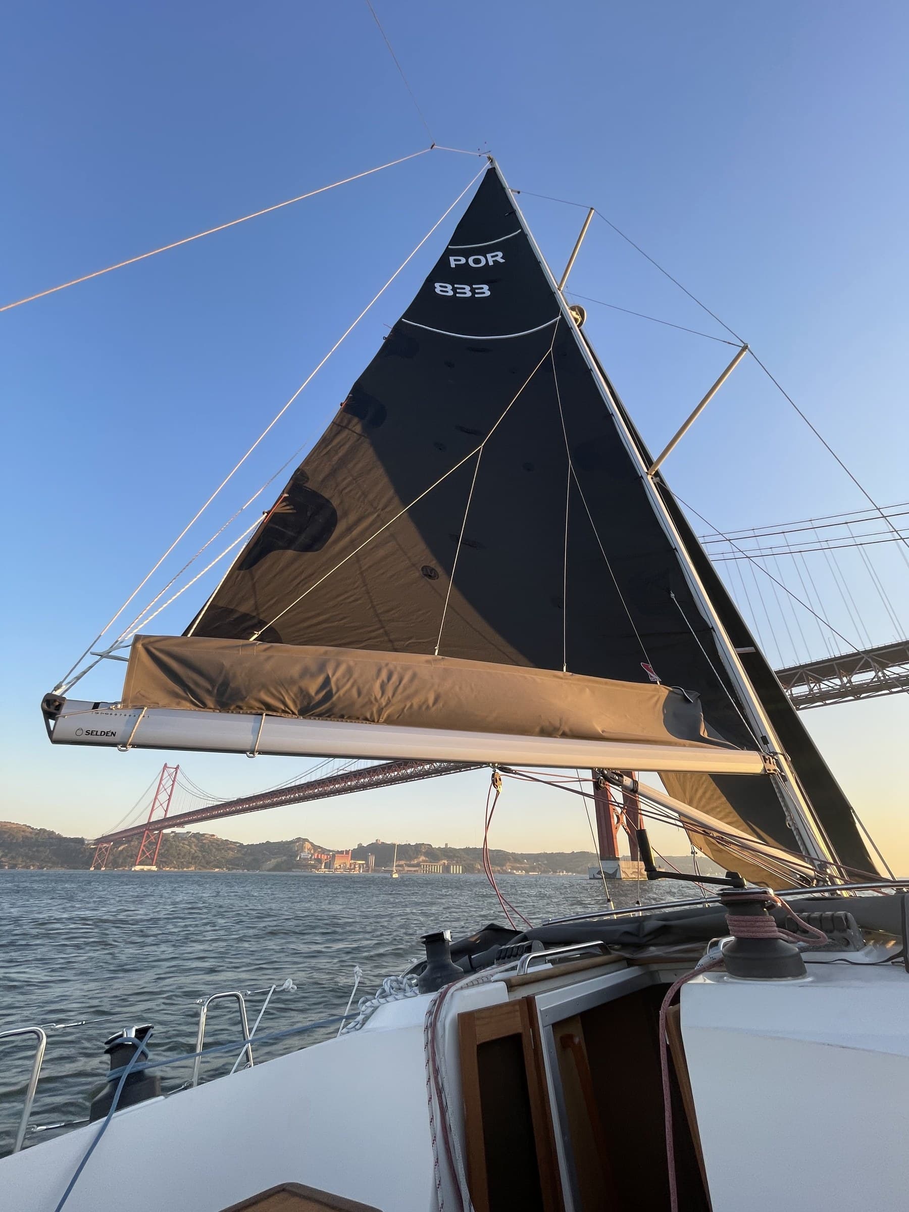 Mainsail framing the 25 de Abril bridge at golden hour